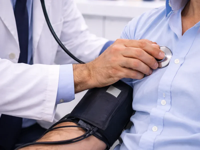 A clinician using a stethoscope during an examination, with a blood-pressure cuff on the seated person's arm
